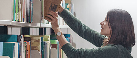 Studentin holt Bücher aus einem Regal in der Bibliothek